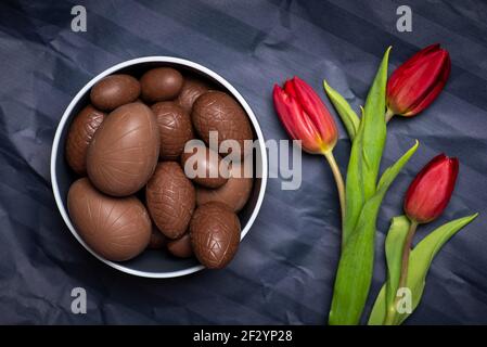 Chocolats œufs de Pâques avec bonbons aux œufs et tulipes rouges arrière-plan papier foncé avec espace de copie Banque D'Images