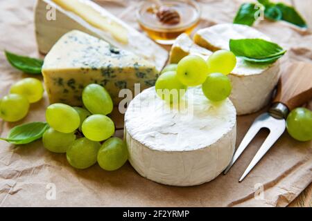 Différents types de fromage, basilic et raisins sur une table Banque D'Images