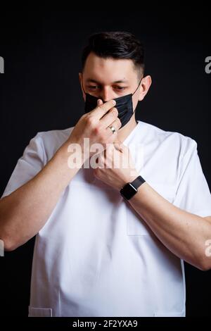 Médecin médecin chef de sexe masculin dans un costume chirurgical blanc. Portrait en gros plan. Porte un masque médical noir contre le virus Banque D'Images