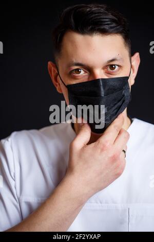 Médecin médecin chef de sexe masculin dans un costume chirurgical blanc. Portrait en gros plan. Porte un masque médical noir contre le virus Banque D'Images