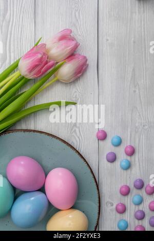 Œufs de Pâques pastel et bonbons au chocolat de couleur avec tulipes blanches roses, sur fond de bois blanc. Banque D'Images
