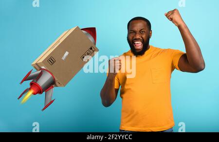 Black man est heureux de recevoir un paquet. Concept de livraison rapide comme une fusée. Fond cyan Banque D'Images