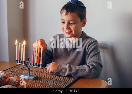 Garçon en kippah éclairant des bougies sur une menorah pour les vacances traditionnelles juives d'hiver Hanukkah. Enfant célébrant le festival des lumières de Chanukah à la maison. REL Banque D'Images