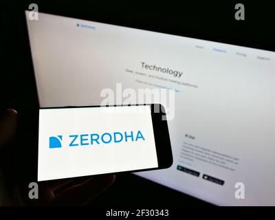Personne tenant un smartphone avec le logo de la société indienne de services financiers Zerodha Broking Ltd. Sur l'écran devant le site Web. Mise au point sur l'affichage du téléphone. Banque D'Images
