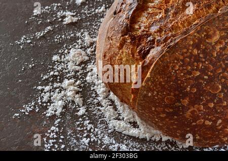 Gros plan de pain maison avec une croûte croustillante sur le table de cuisine arrosée de farine Banque D'Images