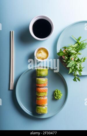 Les sushis japonais se roulent avec de l'avocat et du saumon dans un style minimaliste moderne. Sur fond bleu avec des ombres dures Banque D'Images