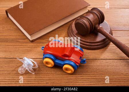 Une sucette, un jouet de voiture, un gavel de juge et un livre sur table en bois Banque D'Images
