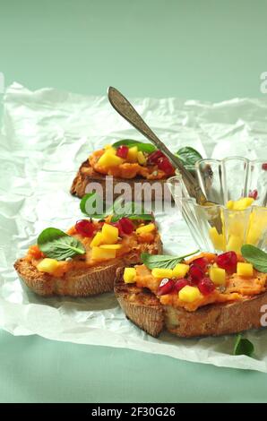 Crostini avec purée de patates douces, mangue, jeunes épinards chinois et grenade Banque D'Images