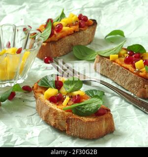 Crostini avec purée de patates douces, mangue, jeunes épinards chinois et grenade Banque D'Images