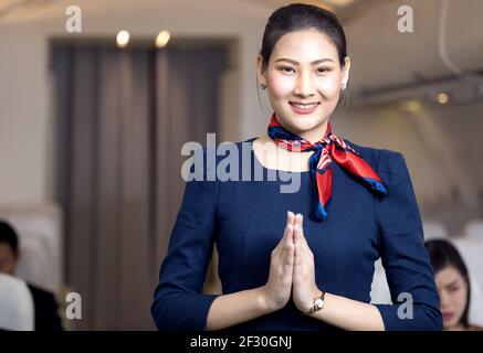 Un agent de bord asiatique se posant avec le sourire au milieu de la allée à l'intérieur du siège passager de l'avion sur l'arrière-plan Banque D'Images