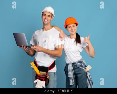 Achat en ligne pour réparation. Couple en casque de sécurité tenant un ordinateur portable montrant le pouce vers le haut Banque D'Images
