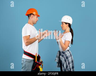 Jeune couple émotionnel en casque de protection ayant malentendu pendant réparation à domicile Banque D'Images