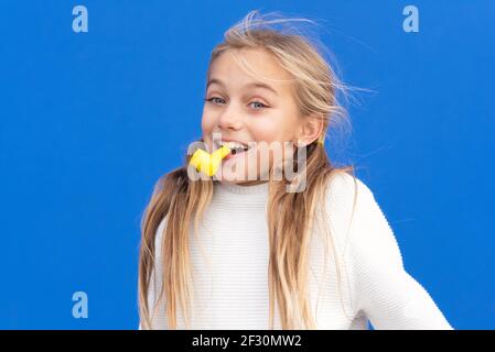 Studio portrait d'une jeune fille heureuse et souriante célébrant la fête d'anniversaire, tenant le souffleur de fête dans la bouche s'amusant, isolé sur le bleu. Photo de haute qualité Banque D'Images