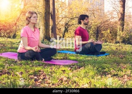 Cours de yoga. Des gens joyeux et paisibles assis dans la posture du lotus tout en pratiquant le yoga à l'extérieur Banque D'Images