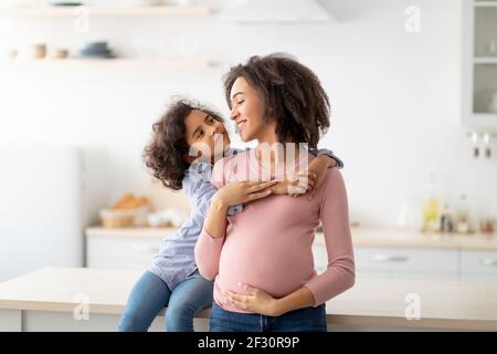 Fille afro-américaine embrassant sa mère enceinte du dos Banque D'Images