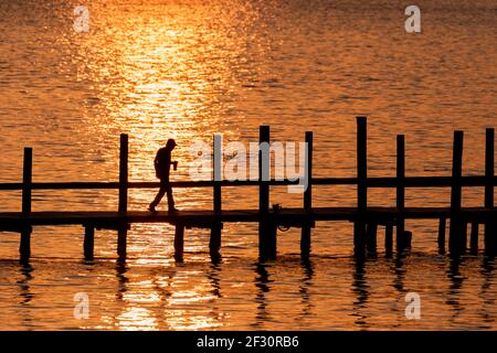 Un homme en silhouette se promène le long d'un quai tandis que le soleil se couche sur Mobile Bay à Fairhope, AL, USA, le 21 octobre 2020. Banque D'Images