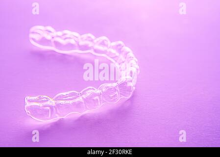 Les dents dentaires invisibles sont des supports d'alignement des dents sur fond violet. Entretoises en plastique, pièces de retenue dentaires pour redresser les dents. Banque D'Images