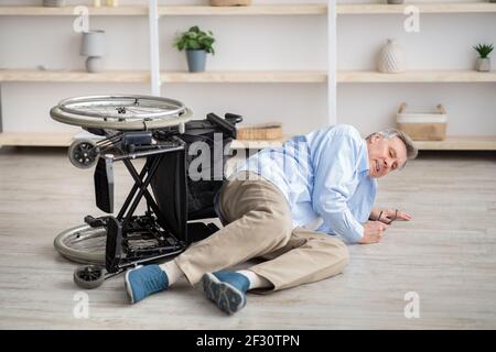 Homme âgé ayant une déficience physique couché sur le sol après une chute en bas de son fauteuil roulant à la maison Banque D'Images