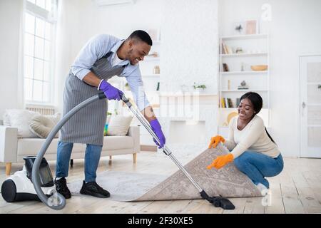 Positif noir couple de nettoyage ensemble, passer l'aspirateur sous la moquette à leur maison, l'espace de copie Banque D'Images