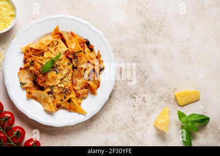 Pâtes Maltagliati avec sauce tomate classique, parmesan et basilic sur fond de table en béton léger rustique. Plats italiens traditionnels. Top vie Banque D'Images