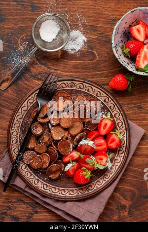 Mini céréales au chocolat et crêpes avec fraises pour le petit déjeuner sur une table en bois. Petit déjeuner à la mode avec de minuscules crêpes. Vue de dessus Banque D'Images