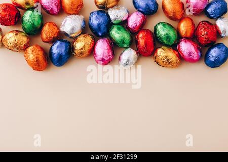 Mini oeufs au chocolat de Pâques enveloppés dans un papier d'aluminium coloré, éparpillés sur un fond beige, vue du dessus, espace copie. Banque D'Images