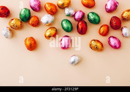 Mini oeufs au chocolat de Pâques enveloppés dans un papier d'aluminium coloré, éparpillés sur un fond beige, vue du dessus, espace copie. Banque D'Images