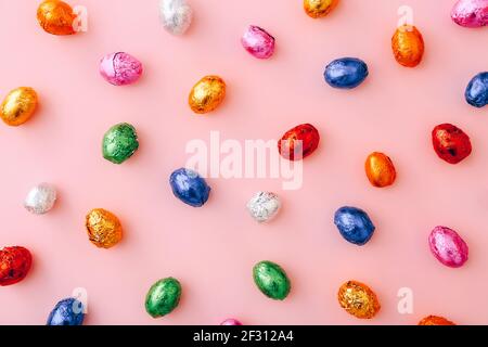 Mini œufs de chocolat de Pâques enveloppés dans un papier d'aluminium coloré, éparpillés sur fond rose Banque D'Images