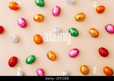 Mini œufs de chocolat de Pâques enveloppés dans un papier d'aluminium coloré, éparpillés sur un fond beige Banque D'Images