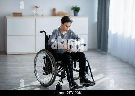 Joueur de football en fauteuil roulant tenant un ballon de football sur toute la longueur balle et sensation de stress sur sa blessure à la maison Banque D'Images