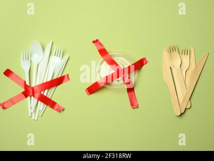 Fourchettes et cuillères en plastique collées avec du ruban rouge sur un fond vert, évitant le plastique Banque D'Images