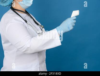 Femme médecin sous une blouse médicale blanche, gants en latex bleu portant un thermomètre électronique sans contact en plastique Banque D'Images