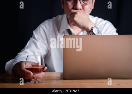 Un homme d'affaires avec un verre à whisky à cause du stress de travailler dur la nuit Banque D'Images