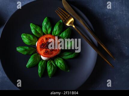 Variété de salade Caprese, tranches de tomates mûres fraîches, mini-mozzarella, feuilles de basilic frais et caviar balsamique. Tableau d'arrière-plan sombre. Gros plan, Banque D'Images