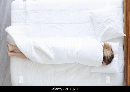 La femme dormant repose sur un lit enveloppé de couverture Banque D'Images