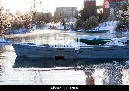 Vieux bateau à rames en bois recouvert de neige sur la rive en hiver. Bateau de pêche. Un lac ou une rivière gelé. Température ambiante basse. La saison de l'hiver Banque D'Images