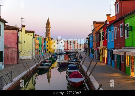 L'île vénitienne de Burano, des bateaux amarrés sur un canal, maison colorée et des boutiques au crépuscule Banque D'Images