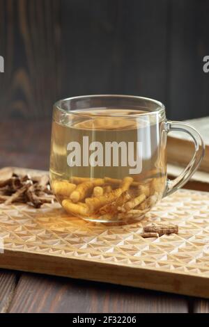 Thé de racine de pissenlit dans une tasse de verre avec racine sèche sur panneau rustique en bois, gros plan, boisson à base de plantes est un remède probiotique et digestif, bon pour le diabète, l'urin Banque D'Images