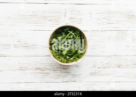 Feuilles de salade d'arugula fraîches vertes dans un bol sur fond de bois blanc. Concept de saine alimentation. Photo de haute qualité Banque D'Images