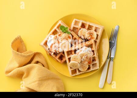 Gaufres belges à la banane au caramel, aux amandes et à la crème. Petit déjeuner sucré avec gaufres belges sur fond jaune Banque D'Images