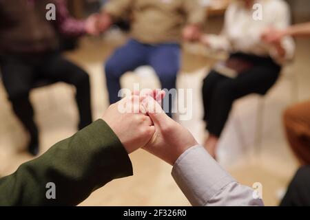 Plusieurs patients interculturels de groupe contemporain de soutien mental tenue par mains pendant la session en étant assis en cercle Banque D'Images