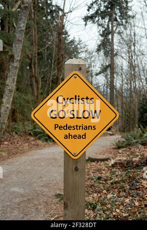 Les cyclistes vont les piétons lents devant un panneau sur un sentier dans le parc régional Pacific Spirit, Vancouver, Colombie-Britannique, Canada Banque D'Images