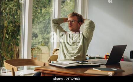 Homme assis à la table avec les mains derrière la tête. Homme prenant une pause en travaillant de chez lui. Banque D'Images