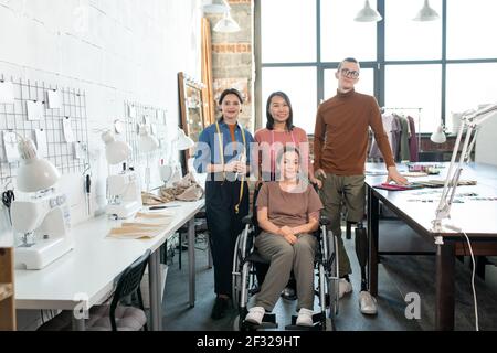 Une équipe de créateurs de mode contemporains et de tailleurs de vêtements décontractés se tenir entre les tables avec l'équipement de travail Banque D'Images