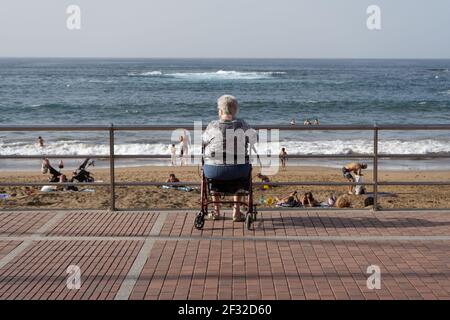 Plage de Las Canteras à Las Palmas de Gran Canaria, Espagne - 19 février 2021 : une femme âgée assise dans son cadre de marche et regardant les gens se baigner sur la Banque D'Images