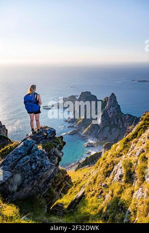 Soleil du soir, randonneur debout sur un rocher, vue sur les falaises dans la mer, au sommet de la montagne de Matinden, près de Stave, Nordland, Norvège Banque D'Images