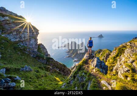 Soleil du soir, randonneur debout sur un rocher, vue sur les falaises dans la mer, au sommet de la montagne de Matinden, près de Stave, Nordland, Norvège Banque D'Images