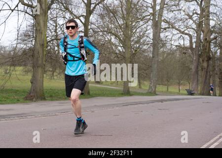 Un coureur de lunettes de soleil avec sac à dos et short noir court à Londres Greenwich Park, Royaume-Uni Banque D'Images