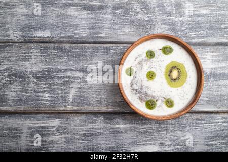 Yaourt avec kiwi, groseille, chia et amandes dans un bol en bois sur fond de bois gris. Vue du dessus, plat, espace copie. Banque D'Images