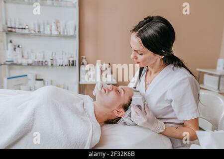 Esthéticienne effectuant la procédure de nettoyage du visage à l'aide d'une spatule à récurer à ultrasons dans un salon de beauté Banque D'Images